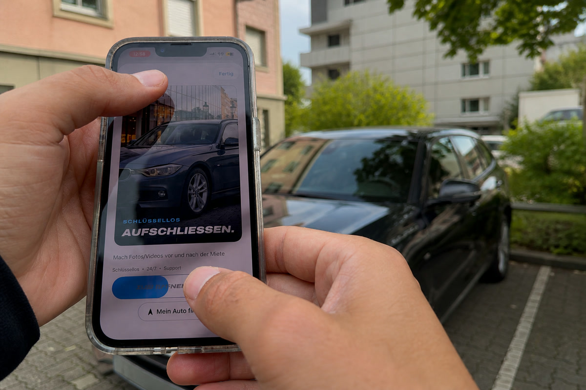 Two hands holding a phone with the DRAIV app open in front of a parked BMW